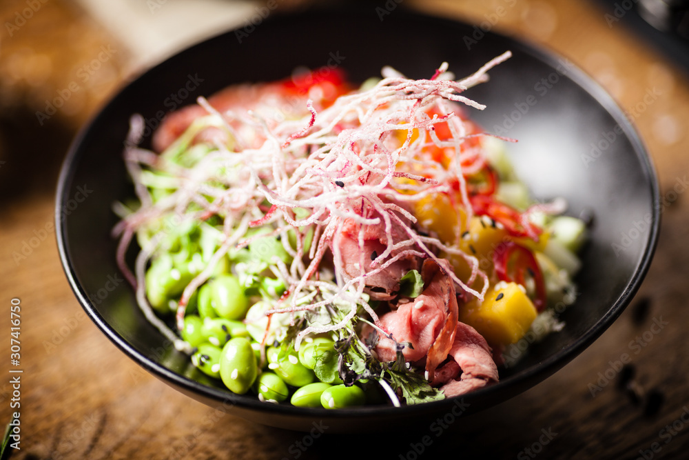 Poke with beef served in a black bowl in restaurant Poke with beef served in a black bowl in restaurant