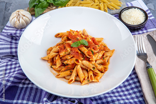 Penne pasta with chili sauce arrabiata. Classic italian penne arrabiata with basil and freshly grated pecorino cheese on a rustic wooden table. photo