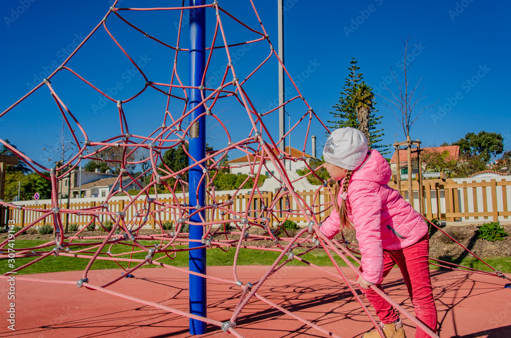 Little girl on a playground climbs upstairs. Child playing outdoors in spring. Happy kid in kindergarten or preschool