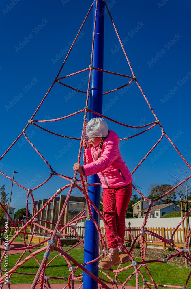Little girl on a playground climbs upstairs. Child playing outdoors in spring. Happy kid in kindergarten or preschool
