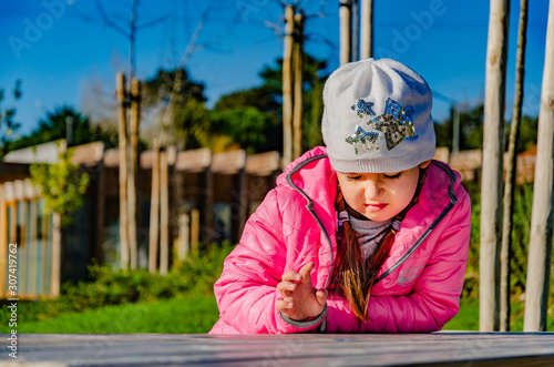 Pensive and dreaming little girl sitting at a table in the park. Portrait. © Liudmila