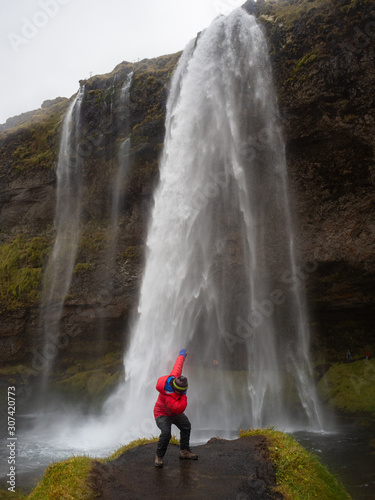 A tourist imitating Usain Bolt in a prominent area on the impressive Seljalandsfoss waterfall. South Coast of Iceland.