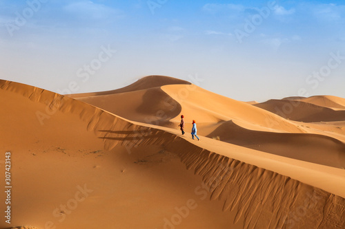 Fototapeta Naklejka Na Ścianę i Meble -  Two Bedouin young men walk across the dunes