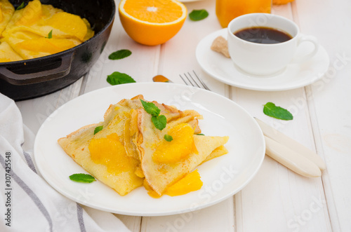 Crepe suzette with orange sauce and a cup of coffee on a white wooden background. Tasty and fragrant breakfast.