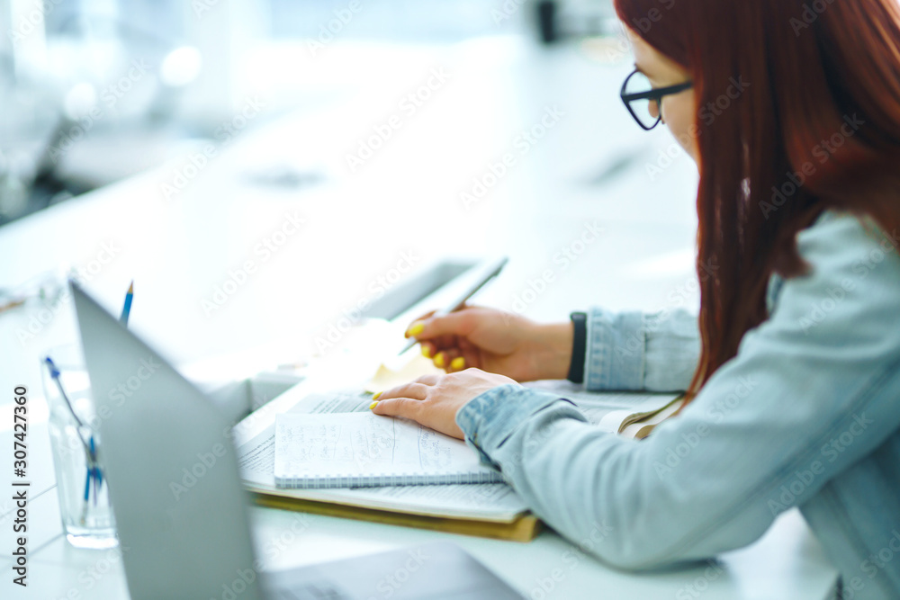 Young woman's hands holding pen and writing in daily planner. Teenager student in a yellow sweater prepares for exams. Freelancer works and makes notes. Startup small business.