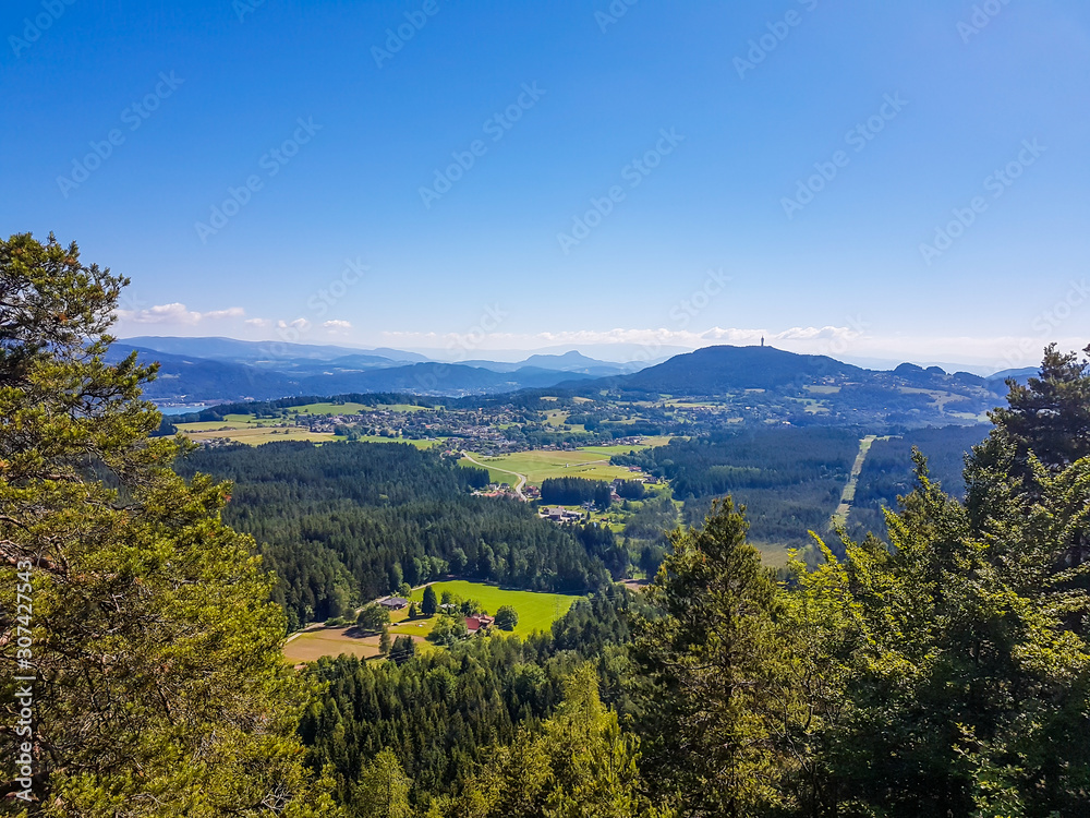 A panoramic, areal view on an alpine landscape of Austria. There are high Alps in the back. Few trees on the side, forming a small forest. Idyllic landscape. There is a tower on one of the mountains.