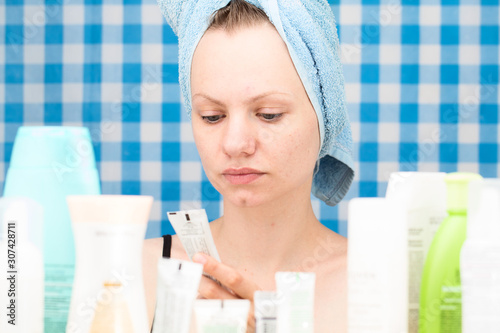 Portrait of girl without makeup in bathroom surrounded by cosmetics