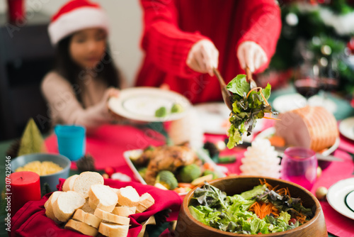 Young Asian family celebration in Christmas day, mother take meal salad to daughter which smiling and felling happy love in kitchen at home in morning time. Merry Xmas.