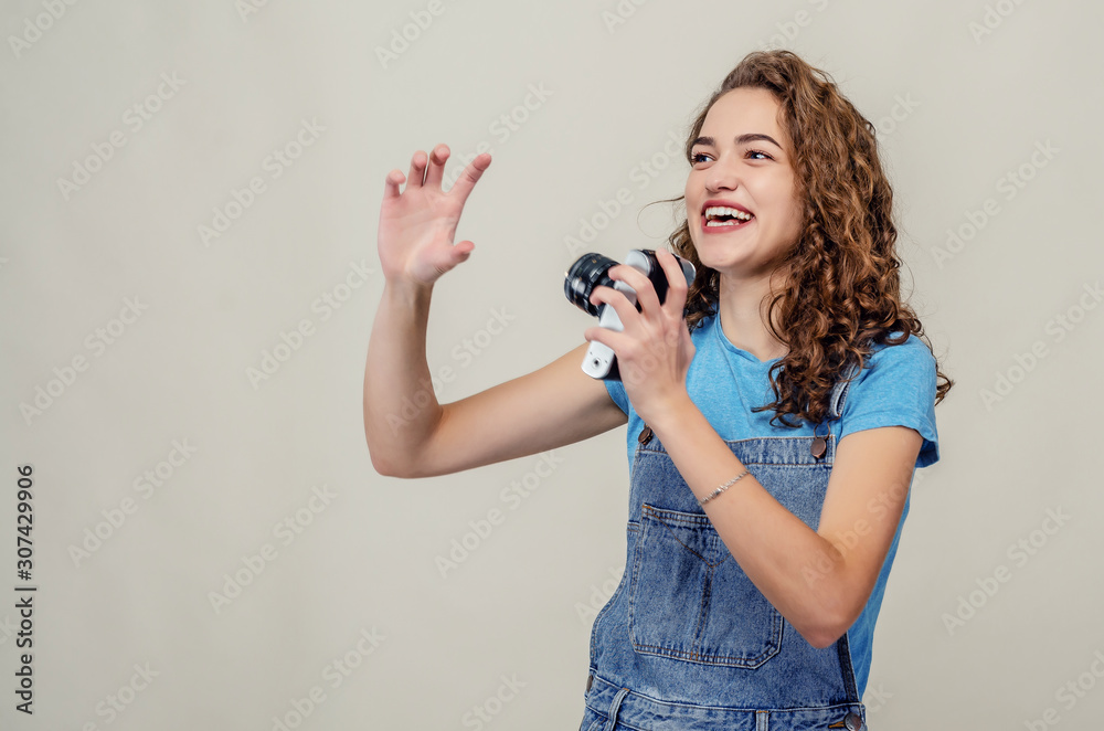 Curly cheerful brunette in denim overalls holds a film camera in her hands, having fun on the set Curly cheerful brunette in denim overalls holds a film camera in her hands, having fun on the set