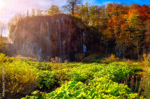 Plitvice lakes (Plitvicka jezera) national park, Croatia. Amazing autumn sunny landscape with waterfall, colored trees and blue sky, Prstavac. Outdoor travel background, famous landmark photo