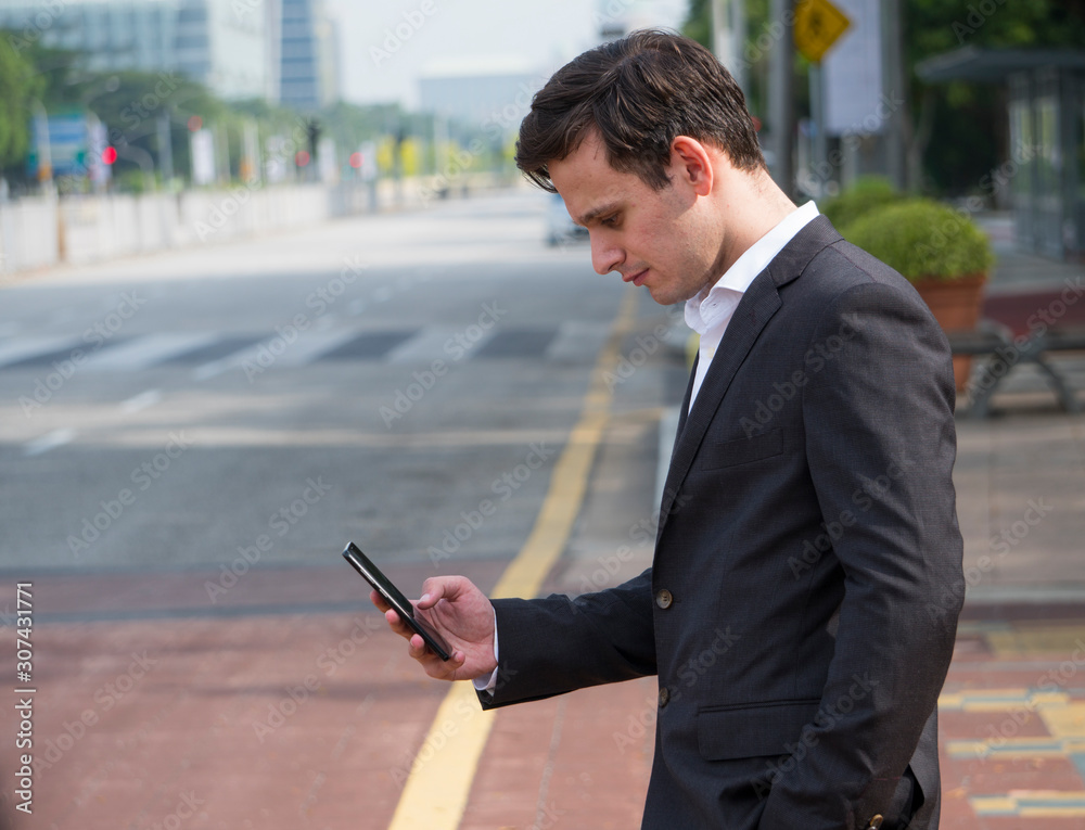 Adult man standing at road side while holding mobile phone. Adult man standing at road side while holding mobile phone.