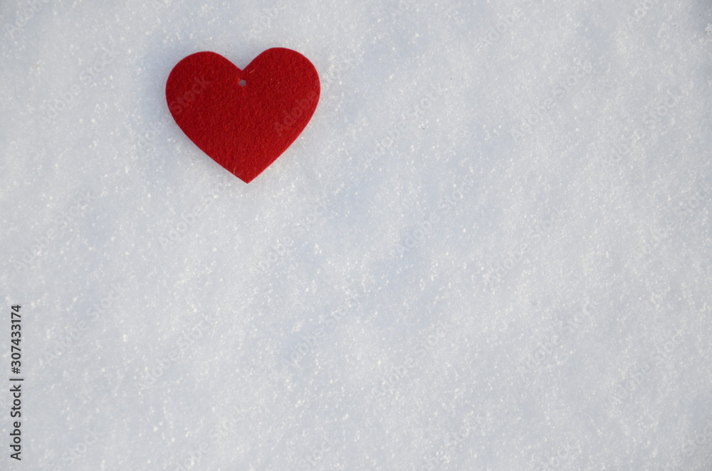 Winter. Holidays. Against the background of white fluffy snow lies a red felt heart.