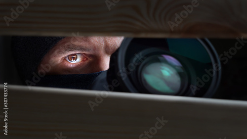 Espionage concept. Privacy idea. Private life. Detective with camera. Man's eye looking through a hole between wooden boards. closeup. Information leak. Public life. Filming under the table