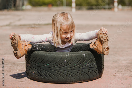 Happy adorable little girl sitting inside car tire while having fun and playing outdoors on summer day photo