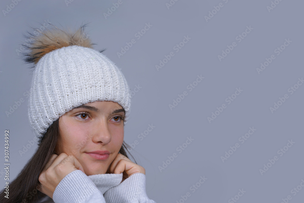 close-up face portrait beautiful young girl wearing in warm knitted white hat and pullover isolated on gray background with copy space, wintertime trendy fashion concept close-up face portrait beautiful young girl wearing in warm knitted white hat and pullover isolated on gray background with copy space, wintertime trendy fashion concept