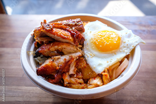A bibimbap bowl of rice topped with grilled chicken slices, egg and kim chi