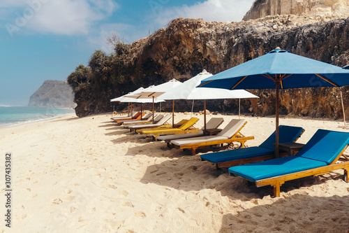 Wooden deck chairs with umbrellas along the coastline. Melasti Beach in the Indian Ocean. Indonesia, Bali.