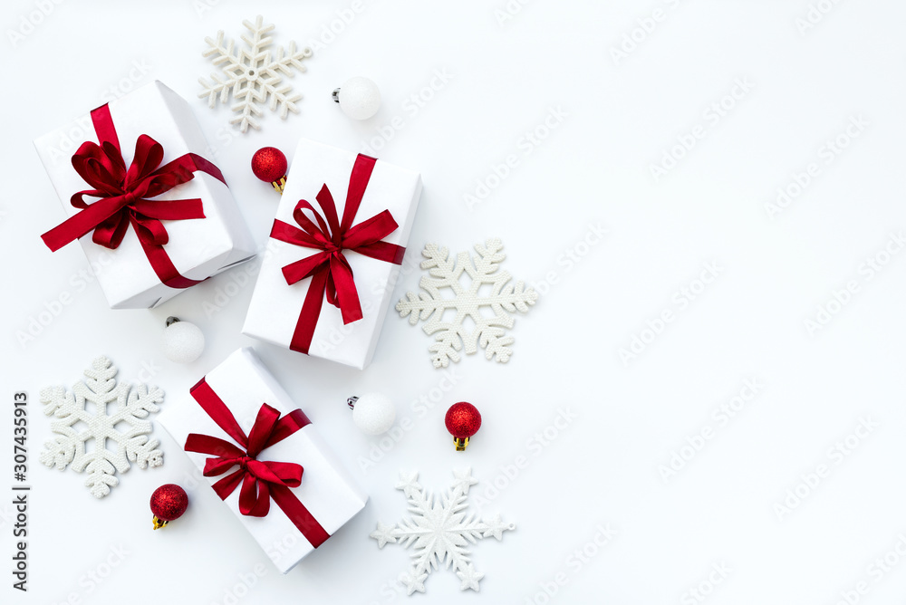 Fototapeta premium Gift boxes wrapped white paper and red ribbon decorated baubles and snowflakes on white background. Top view. Flat lay. Christmas and New Year