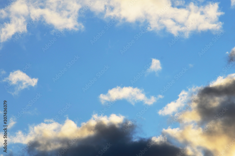 Fototapeta premium In the blue sky, white and dark clouds. The sun illuminates the clouds. Evening sky. 