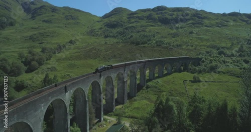 Wide aerial of the Hogwart's Express (Harry Potter) steam train travelling over the Glen Finnan Viaduct in the Scottish Highlands on a sunny day photo