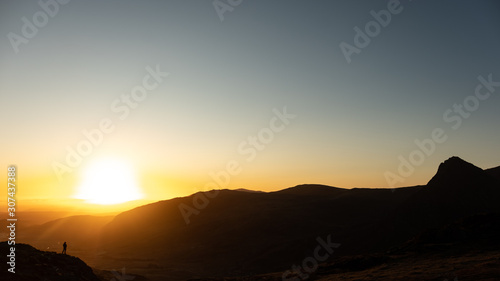 A hiker silhouetted against beautiful orange sunrise in mountains