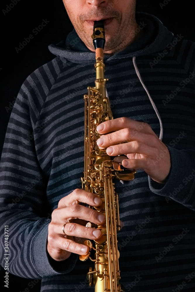Naklejka premium soprano saxophone in the hands of a guy on a black background