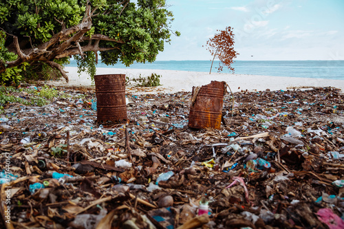 Dump and Washed Up Waste, Debries, Plastic Bottles & Bags, Iron Barrels on a Sandy Beach in Maldives. Blue Sky, Ocean, Paradise. Sunny Side of Life photo