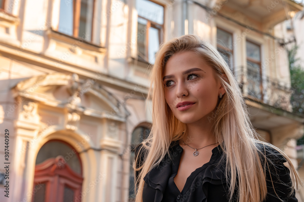 Waist up portrait of attractive stylish blonde woman with loose hair walks among old city center