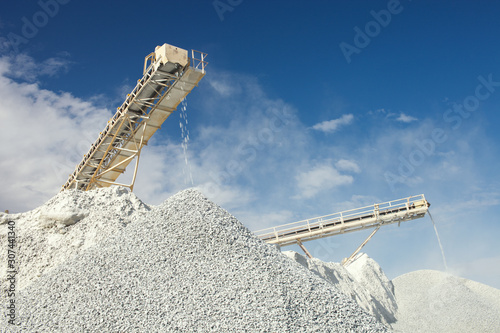 Conveyor belt at the equipment for crushing and sorting rocks into fractions at a mining enterprise on the background of the blue sky with clouds.