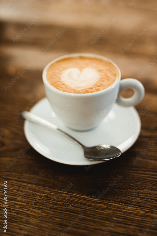 Cup of fresh cappuccino with heart shape on froth served on wooden table in cafe Cup of fresh cappuccino with heart shape on froth served on wooden table in cafe