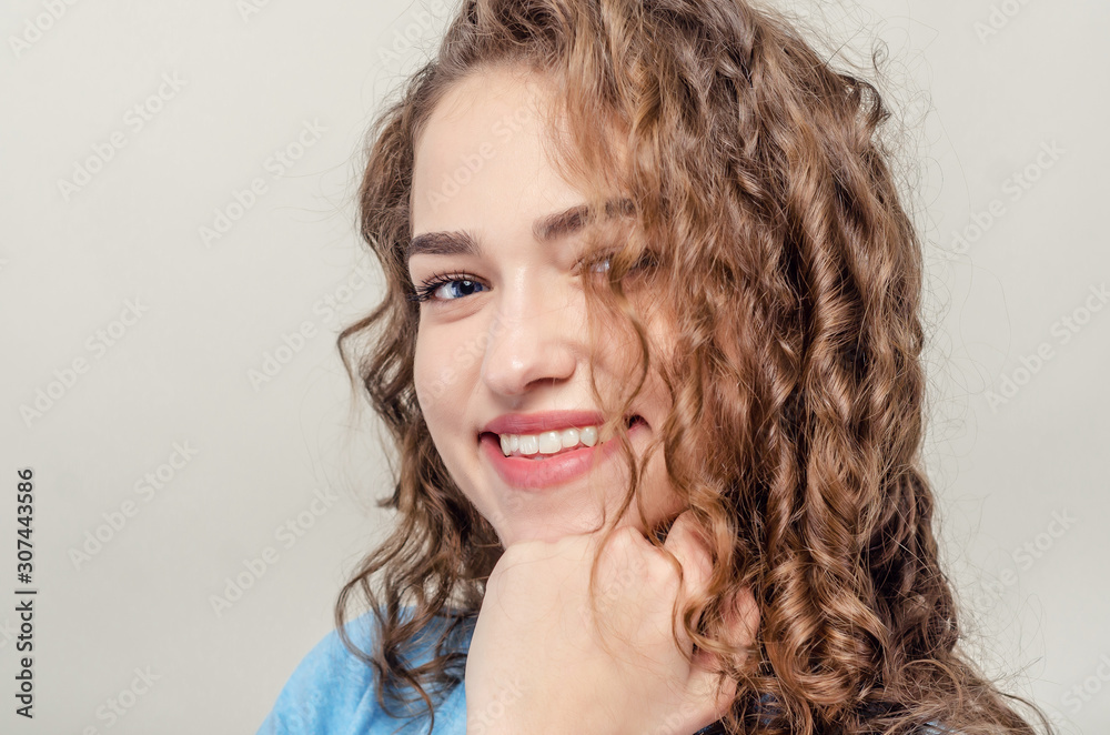 Portrait of beautiful young girl, close-up. Curly hair. Playing hair. Seductive smile Portrait of beautiful young girl, close-up. Curly hair. Playing hair. Seductive smile