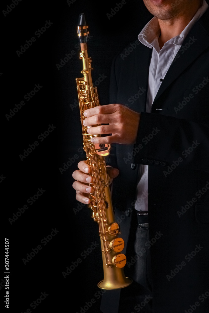 Naklejka premium soprano saxophone in the hands of a guy on a black background
