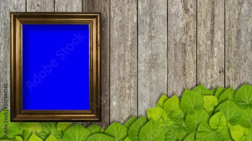 Blank picture frame on wooden wall with green leaves