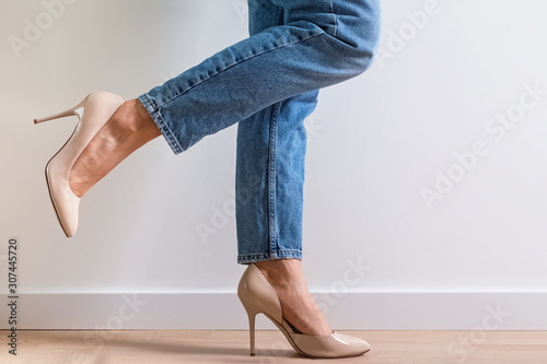 Obraz na płótnie Woman dressed in denim pants and high heels standing near the white wall with one leg raised