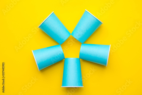 Pattern from blue paper disposable cups on yellow background. Set for party. Top view. Minimalist Style. Copy, empty space for text