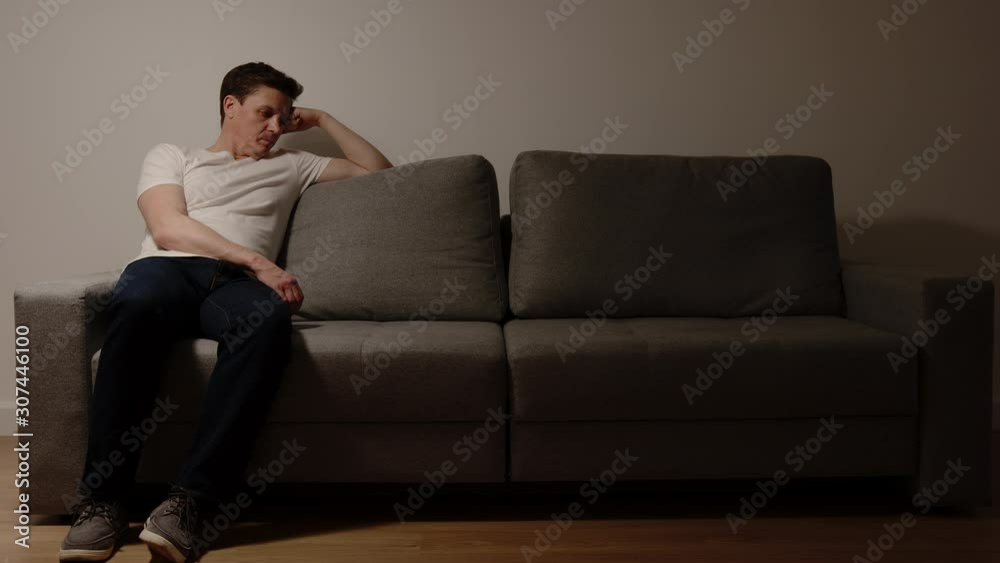 DEPRESSION: Young adult man thinking on a grey sofa in the night DEPRESSION: Young adult man thinking on a grey sofa in the night