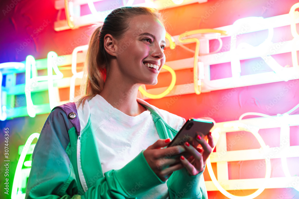 Image of beautiful woman holding smartphone over neon text sign Image of beautiful woman holding smartphone over neon text sign