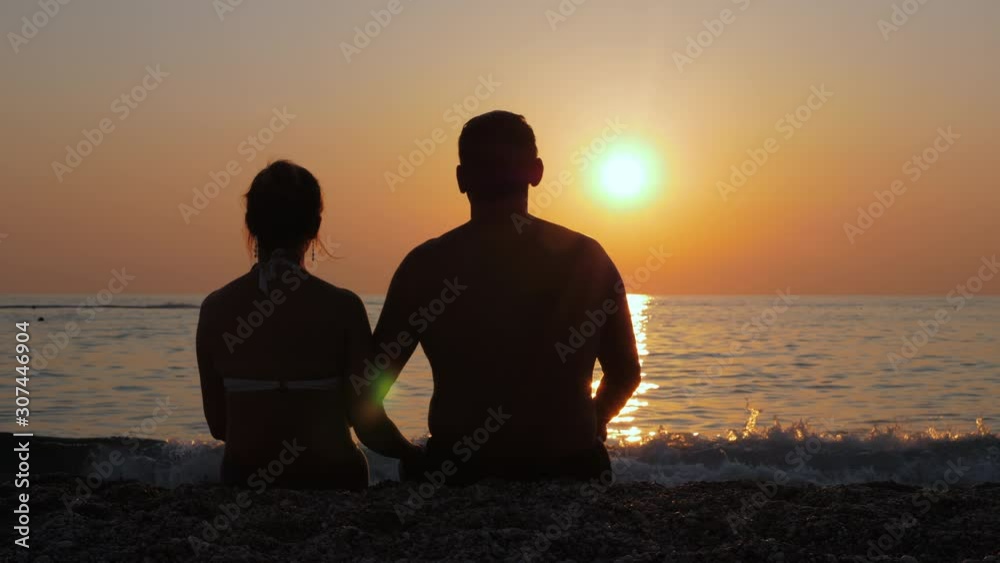 A man and a woman are sitting on the seashore and watching the colorful sunset. Beautiful natural landscape. Happy married couple. A man and a woman are sitting on the seashore and watching the colorful sunset. Beautiful natural landscape. Happy married couple.