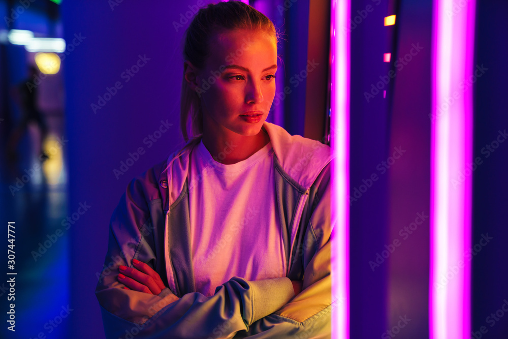 Image of young woman standing by multicolored neon illumination indoors Image of young woman standing by multicolored neon illumination indoors