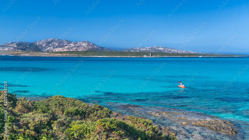 Panoramic view of La Pelosa beach in Stintino, turquoise clear water, mountains in the background. Kayaking in the sea. Sassari, Sardinia, Italy.
