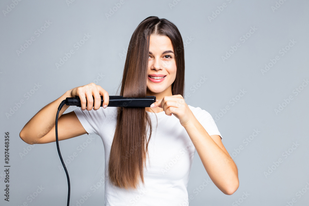 Smiling young woman straightening her hair with white background Smiling young woman straightening her hair with white background