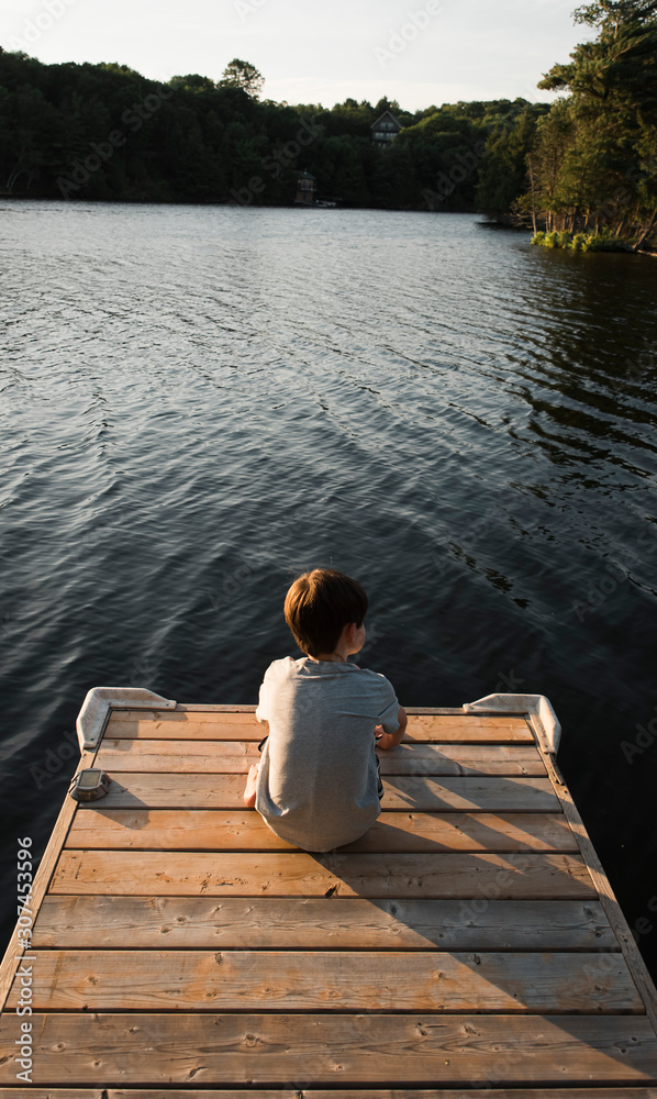 Young boy sitting on the end of a dock on a lake on a summer evening. Young boy sitting on the end of a dock on a lake on a summer evening.