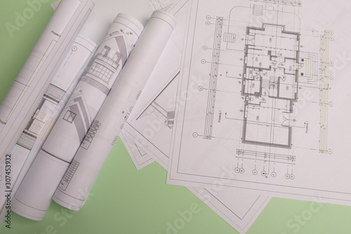 White family paper house , stack of money coins, house projects plan and blueprints on mint background paper. Minimalistic and simple concept, style. Vertical orientation.