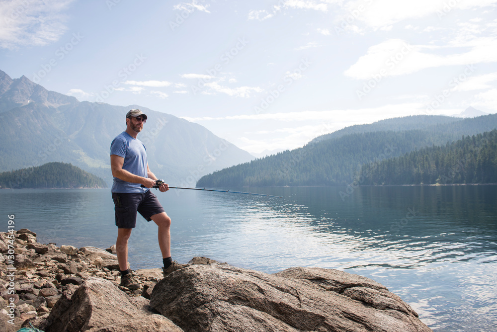 Man standing on rock fishing at Ross Lake in Washington State Man standing on rock fishing at Ross Lake in Washington State