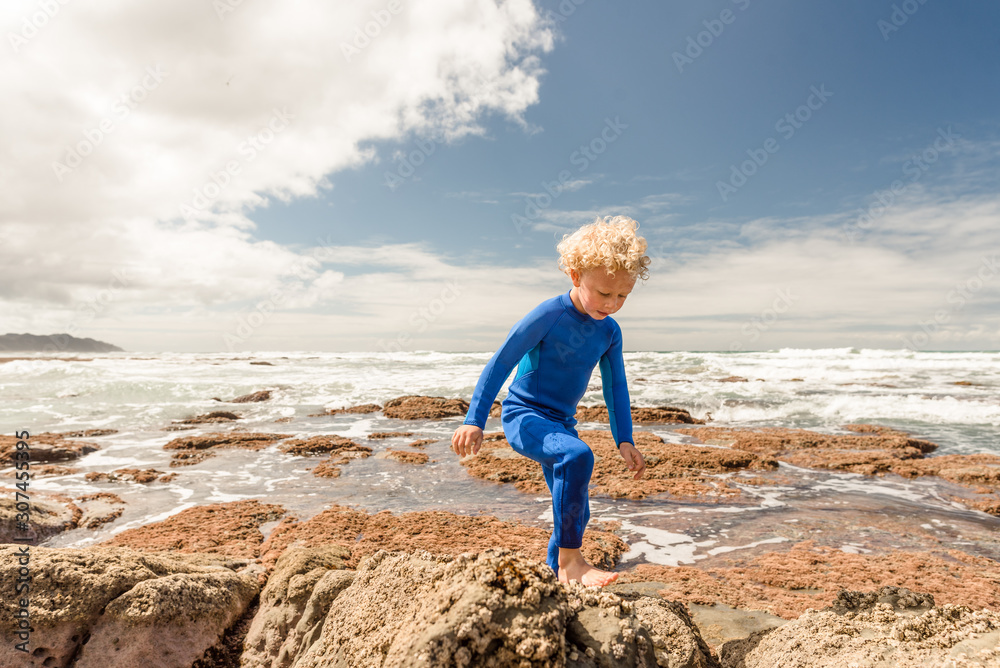 Little boy in blue wetsuit climbing rocks at a beach Little boy in blue wetsuit climbing rocks at a beach