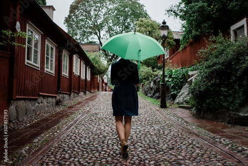 the back of a woman walking up a cobbled street with an umbrella