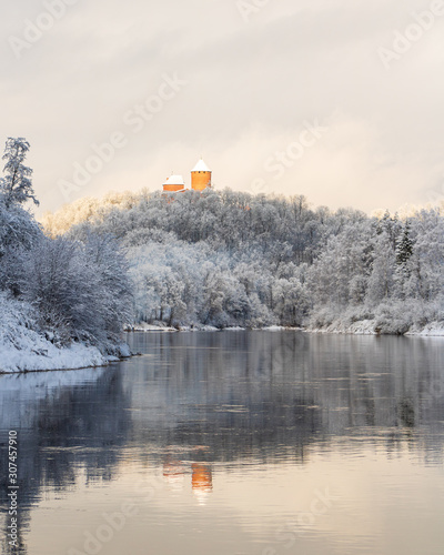 View to ancient Turaida castle standing in snowy trees with river Gauja in foreground on a beautiful winter day in December in Sigulda in Latvia