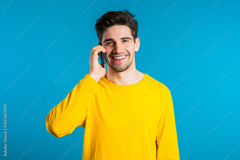 Young man in bright colorful wear talking on mobile cell phone on blue background. Trendy guy have conversation. Smartphone, technology concept. Young man in bright colorful wear talking on mobile cell phone on blue background. Trendy guy have conversation. Smartphone, technology concept.