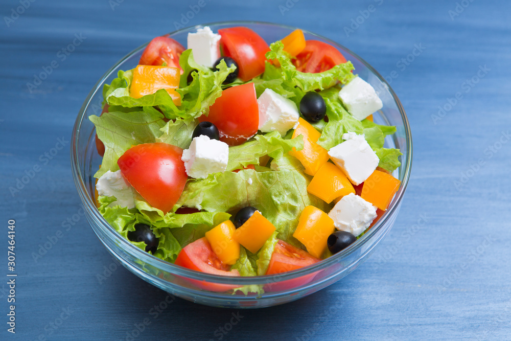 Greek salad in glass bowl on dark gray wooden or metal table