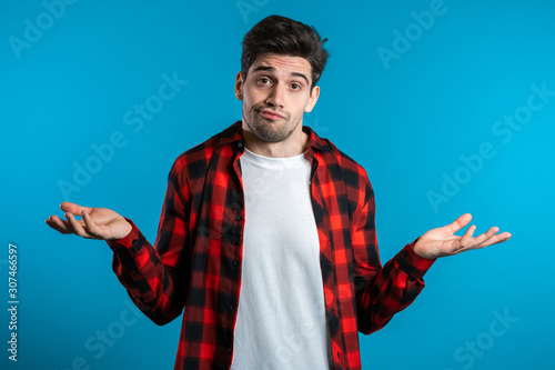 Canvastavla Young handsome unsure guy in red plaid shirt shrugs his arms, makes gesture of I don't know, can't help anything